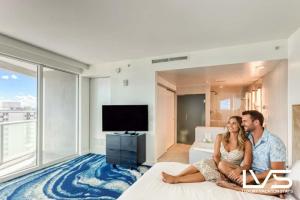Ein Mann und eine Frau sitzen auf einem Bett in einem Hotelzimmer in der Unterkunft W FTL 1409 Beachfront Resort 2 Bedroom & 2 Bathroom Condo in Fort Lauderdale