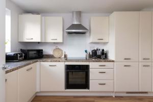 a kitchen with white cabinets and a black oven at Coastal Home for 6 in The Witterings in East Wittering