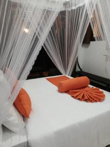 a bed with white curtains and orange pillows on it at Ameliora Hotel Ella in Ella