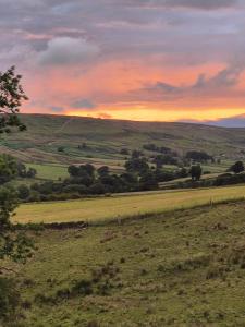 een uitzicht op een veld met een zonsondergang op de achtergrond bij Craven Garth Cottages in Rosedale Abbey
