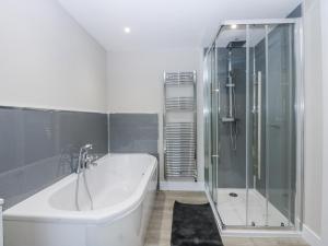 a white bathroom with a tub and a glass shower at Caledfryn in Benllech +10 photos