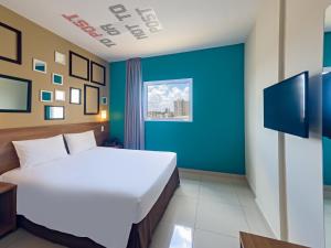 a bedroom with a white bed and a blue wall at Golden Tower Express Braz Olaia by Fênix Hotéis in Ribeirão Preto