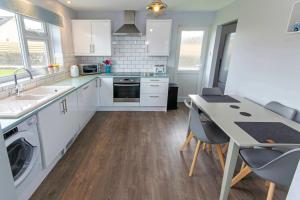 Una cocina con gabinetes blancos y una mesa con sillas. en Sandbanks Braunton, Stylish Cottage near to Saunton Beach Sleeps 4, en Croyde