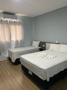 two beds in a room with white sheets at Hotel Sol Nascente in Assaí