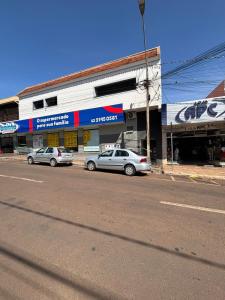 twee auto's geparkeerd voor een winkel in een straat bij Apartamento no Centro de Bandeirantes Ar, TV Smart, Ar Condicionado e Frigobar in Bandeirantes