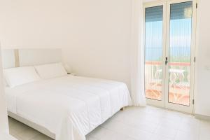 a white bedroom with a bed and a balcony at Aria di sale B&B in Marina di Strongoli