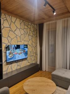 - un salon avec une télévision sur un mur en pierre dans l'établissement Royal Garden Centar apartmani, à Zlatibor