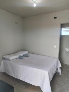 a white bedroom with a bed with two shoes on it at Pousada degamix in Barroquinha