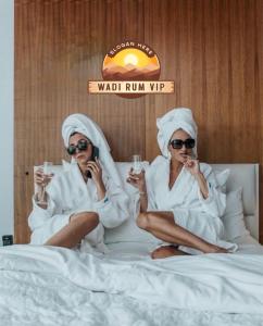 two women in towels sitting on a bed with drinks at WADI RUM NEOM lUXURY CAMP in Wadi Rum