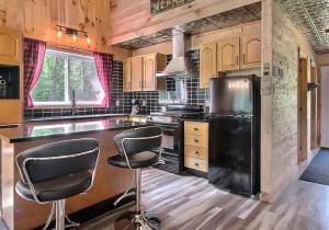 eine Küche mit einem schwarzen Kühlschrank und zwei Barhockern in der Unterkunft Chalet COEUR de loup avec spa in Saint-Alexis-des-Monts