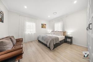 Un dormitorio blanco con una cama y un sofá. en KozyGuru | Erina | Sunny Coastal Escape + Parking, en Erina East