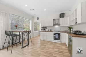 Una cocina con gabinetes blancos y una mesa y sillas. en KozyGuru | Erina | Sunny Coastal Escape + Parking, en Erina East 10 fotos más