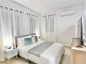 a white bedroom with a bed and a flat screen tv at Rich Villa Guesthouse in Bayamon