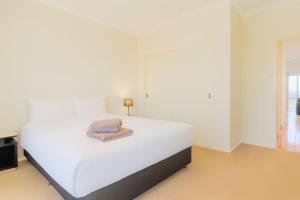 a white bedroom with a bed with a towel on it at Modern 2BR Townhouse with BBQ & Pool Access in Muswellbrook