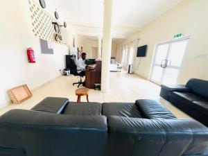 a living room with a black couch and a man in a desk at Mar Luther Inn in Aburi