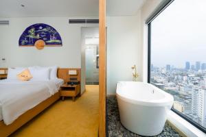 a bedroom with a tub and a bed and a window at Sala Danang Beach Hotel in Danang