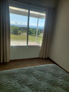 een slaapkamer met een groot raam met uitzicht op een veld bij Bosquemolinos in Villa Los Molinos