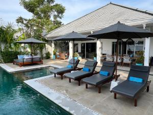 een groep stoelen en parasols naast een zwembad bij Villa Serenity Beachfront Bali in Pengastulan