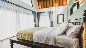 a bedroom with a bed with white sheets and windows at Asri loka villa in Ubud