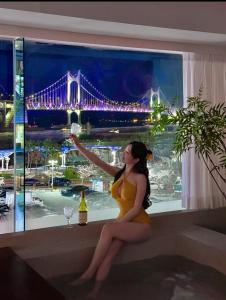 a woman in a yellow dress sitting on a ledge with a view of a bridge at 광안사계스테이 GwanganSagyeStay in Busan