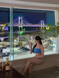 a woman sitting in a window with a view of a bridge at 광안사계스테이 GwanganSagyeStay in Busan
