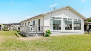 a white house with a porch and large windows at Waterfront, Renovated, Walk To Ettalong in Pretty Beach