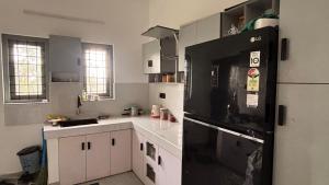 a kitchen with white cabinets and a black refrigerator at Thanal in Trivandrum