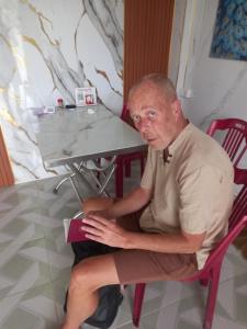 an older man sitting in a chair holding a book at Mai homestay in Mỹ Lại (5)