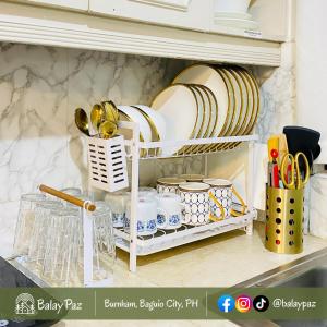 ein Regal in einer Küche mit Tellern und Küchenutensilien in der Unterkunft City View 2BR Home in Burnham - Dalisay Unit by Balay Paz in Baguio City