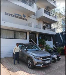 a man standing next to a car in front of a building at Hotel International, Kolhapur in Kolhapur