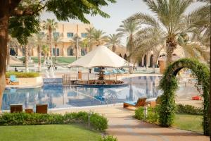 a resort pool with a fountain and palm trees at Metropolitan Al Mafraq Hotel in Abu Dhabi