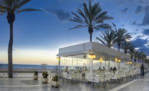 a restaurant with white tables and palm trees on the beach at Expoholidays Almería Centro PARKING gratis in Almería