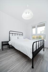 una camera bianca con un letto nero e un lampadario a braccio di Widzewska Prime Apartments by BookingHost a Łódź