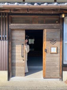 een vrouw die in een houten deur staat bij HANARE紡舎Tsumugiya in Ogawa