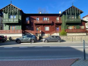 Dos coches estacionados en un estacionamiento frente a un edificio. en Diament Apartment, en Krynica-Zdrój