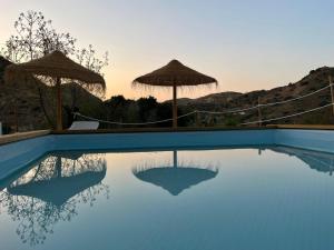 a blue swimming pool with umbrellas and the sunset at Glamping Cabaña Suite Los Almendros in Málaga
