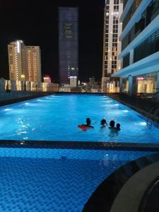three people swimming in a large swimming pool at night at FLC Sea Tower - Sea view Quy Nhơn in Quy Nhon