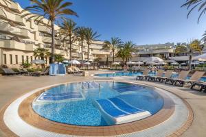 a pool with chairs and palm trees in a resort at Barceló Corralejo Bay - Adults Only in Corralejo