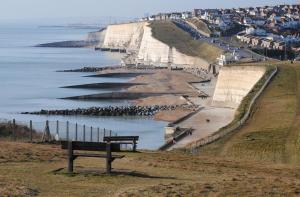 a bench sitting on a hill next to the ocean at 4 Bedroom House in Saltdean, Brighton in Brighton & Hove