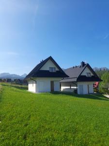 a house with a black roof on a green field at Domki nad Borem in Male Ciche