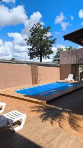 a swimming pool with two white chairs and a tree at Lindo espaço de lazer in Cascavel