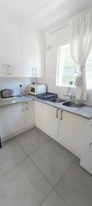 een keuken met witte kasten, een gootsteen en een raam bij Muizenberg lakeside in Lakeside