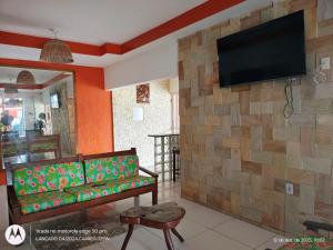 een woonkamer met een tv tegen een stenen muur bij Pousada Meu Xodó in São Miguel dos Milagres