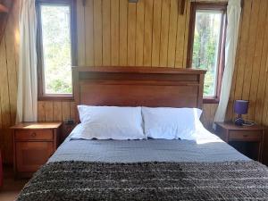 a bedroom with a bed with a wooden headboard and two windows at Cabañas CyG - Chaitén in Chaitén