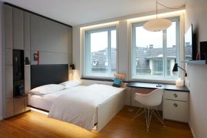 a bedroom with a bed and a desk and two windows at citizenM Zürich in Zürich +18 photos