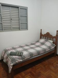 a bed with a plaid blanket and a window at Home office solteiro aconchegante no Centro de Poços de Caldas in Poços de Caldas