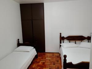 two beds in a room with white walls and wooden floors at Hotel Linassi in Cruz Alta