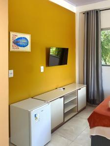 a room with a refrigerator and a tv on a yellow wall at Suítes Preguiça in Sao Jorge