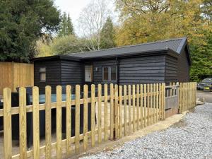 ein schwarzes Haus mit einem Holzzaun davor in der Unterkunft Blackwood - Peaceful cottage surround by woodlands in Byfleet