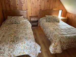 two beds in a room with wooden walls at Casa Rukalma Estación in Villarrica